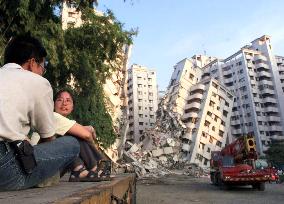 Residents sit resigned in front of collapsed apartments